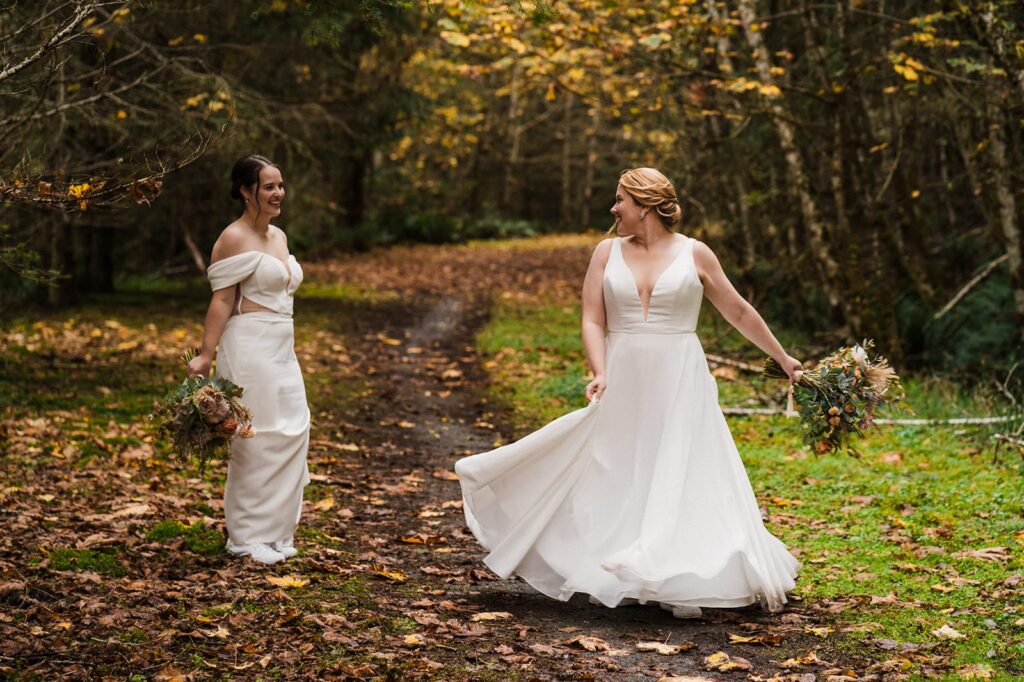 Bride twirls around on in her white forest elopement dress while her bride smiles and watches from the side.