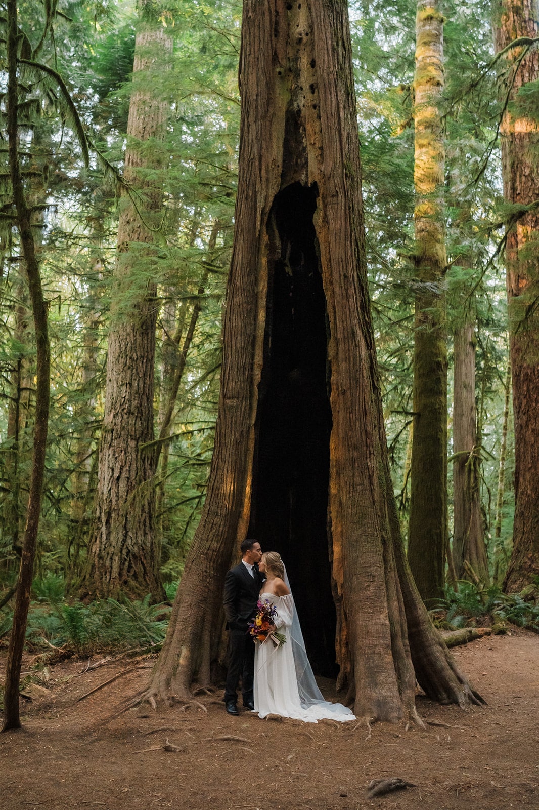 Groom kisses bride on the forehead during their forest elopement. 