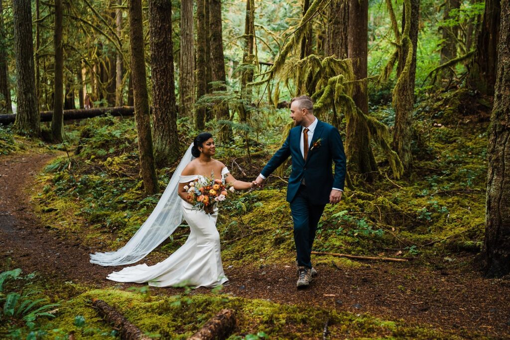 Bride and groom hold hands while walking through a forest trail during their elopement in Washington.