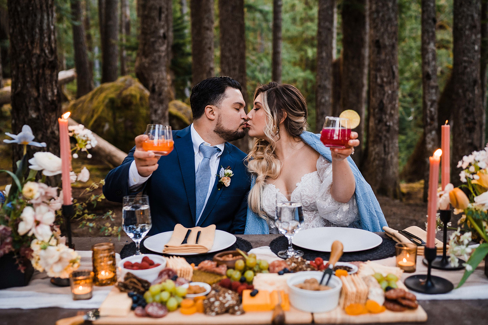 Bride and groom kiss during their celebratory wedding reception meal in the forest during their elopement.