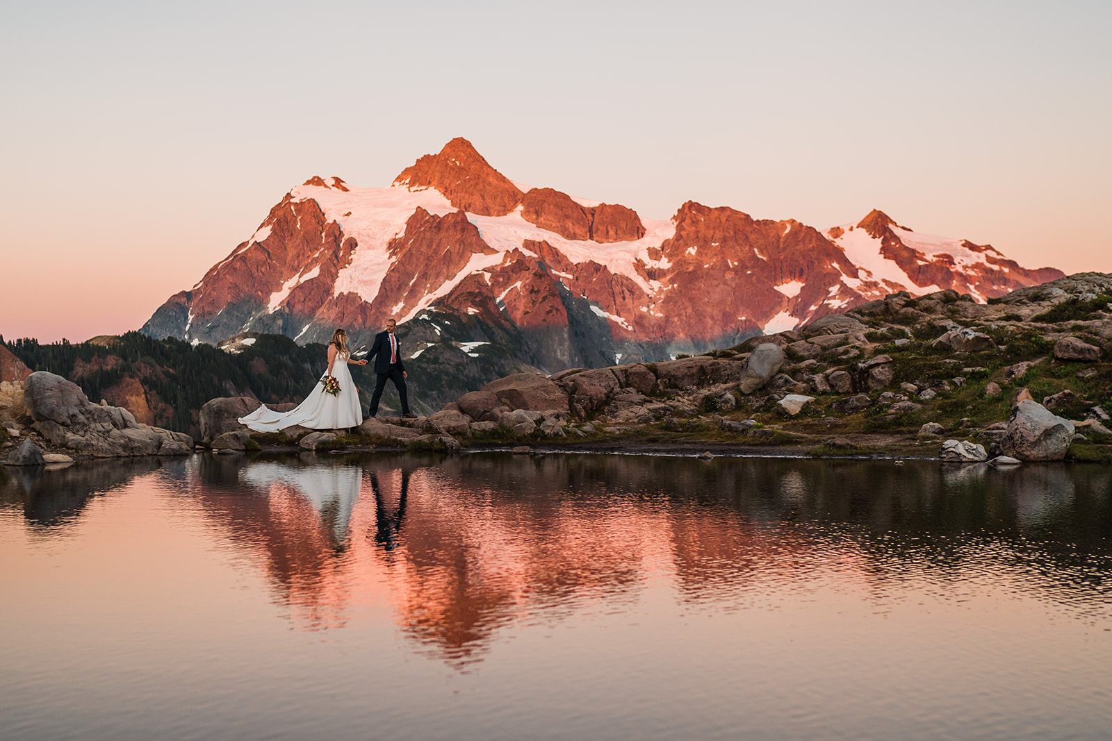 Bride and groom hold hands while walking around a picturesque alpine lake during their elopement in Washington