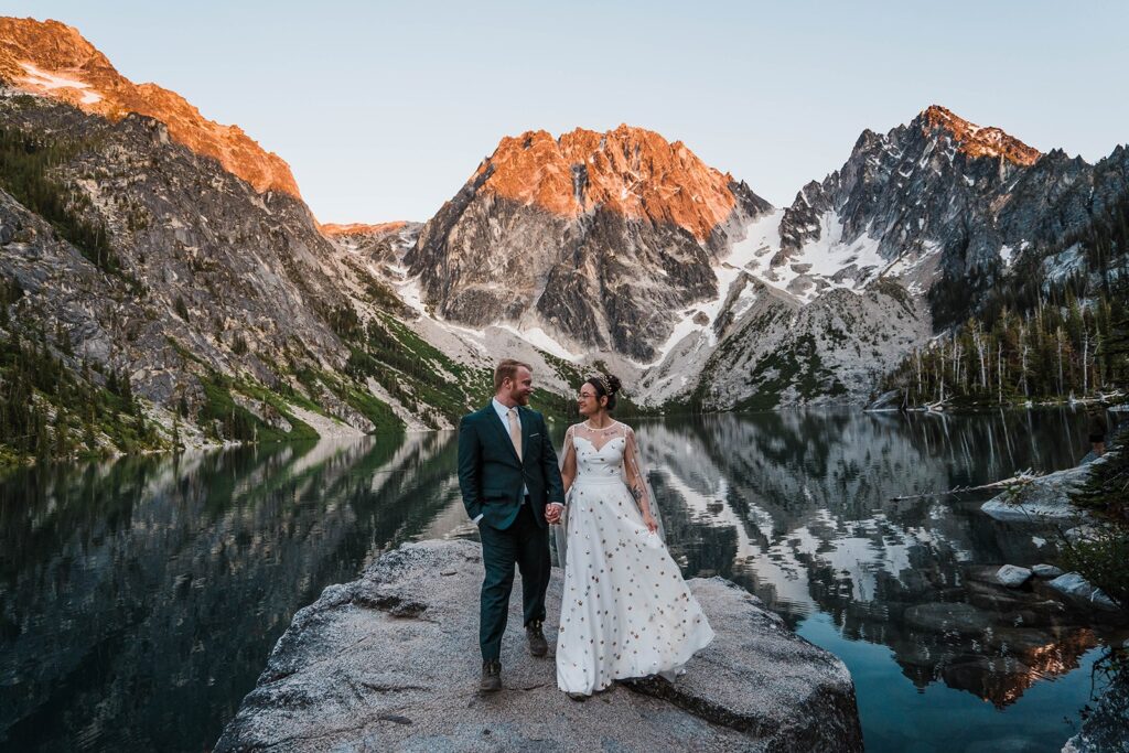 Couple holding hands and standing on a rock in front of a lake in Leavenworth during their Washington state elopement