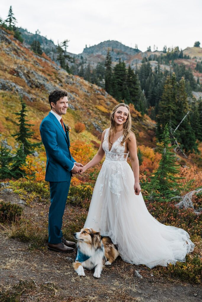 Bride and groom holding hands and smiling while their pup lays down at their feet