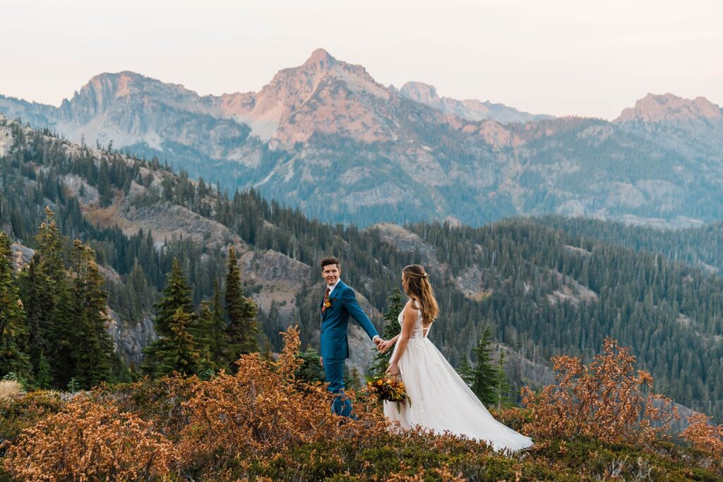 Bride and groom hold hands while walking across the Snoqualmie Pass mountains during sunset photos at their Washington elopement