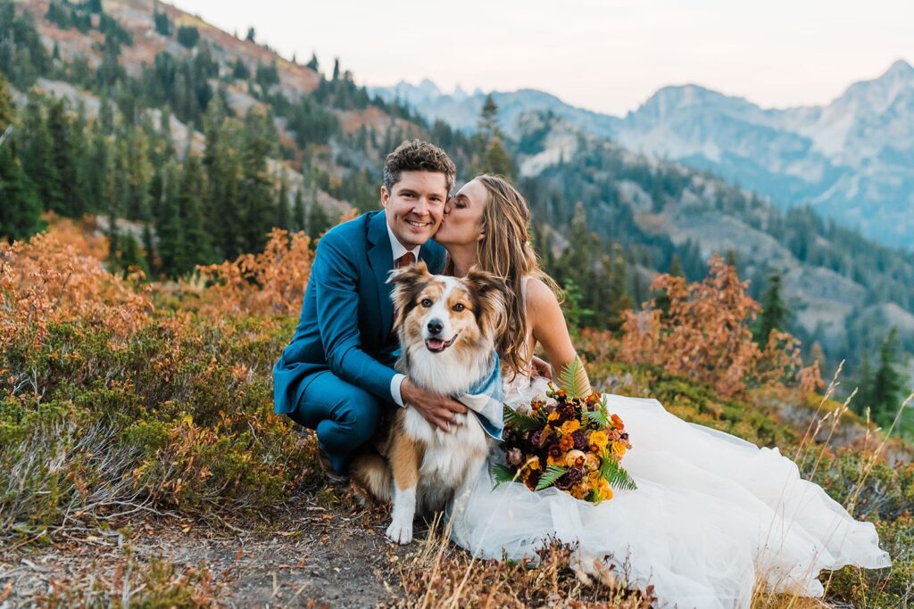 Bride kisses groom on the cheek while posing with their dog at their Snoqualmie Pass elopement