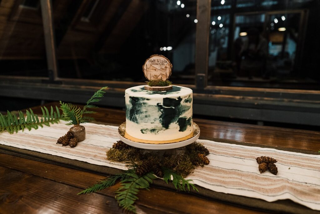 White and green wedding cake with fern, pinecones, and wood decorations