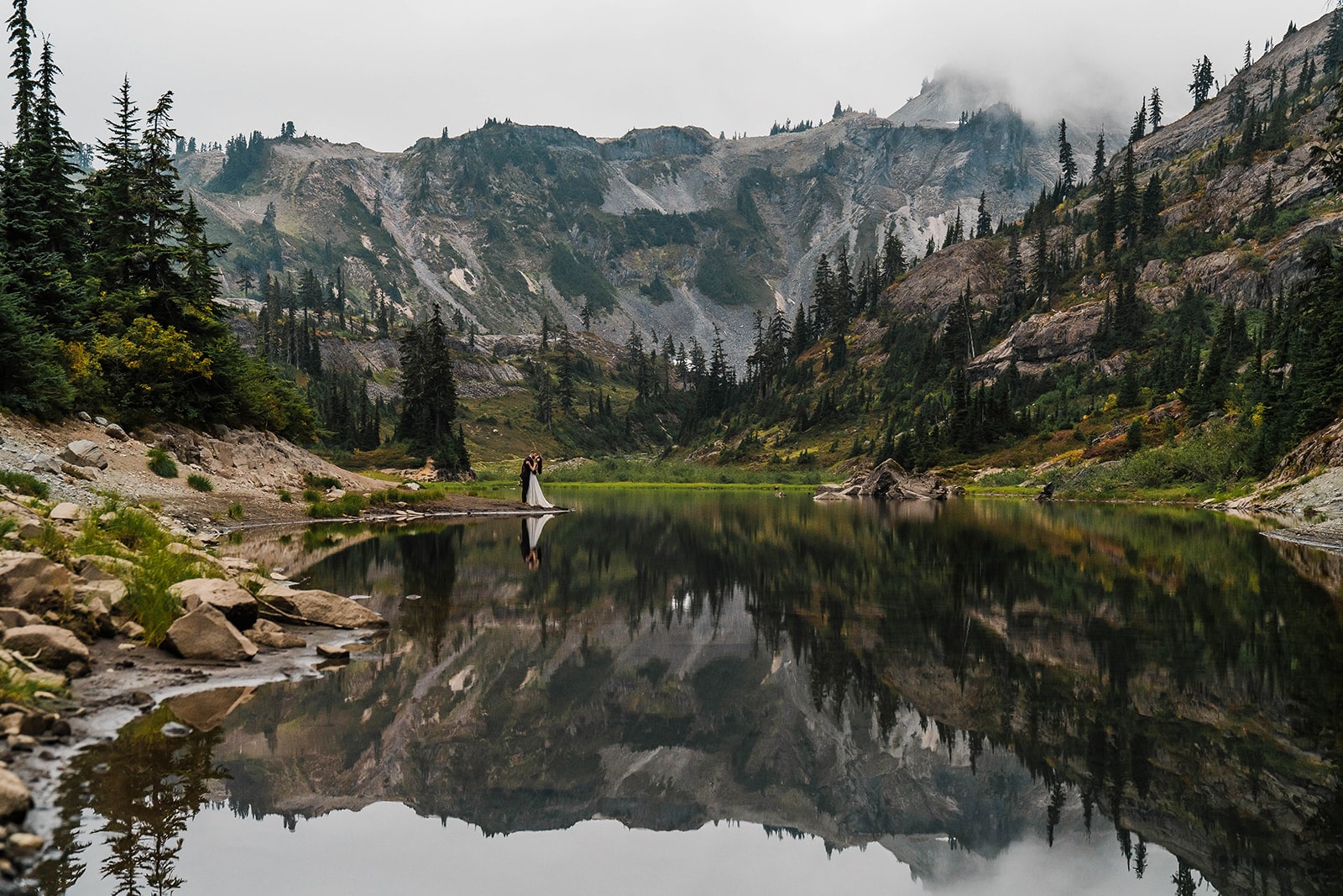 Bride and groom stand at the edge of an alpine lake in the North Cascades, one of the best elopement locations in Washington State.
