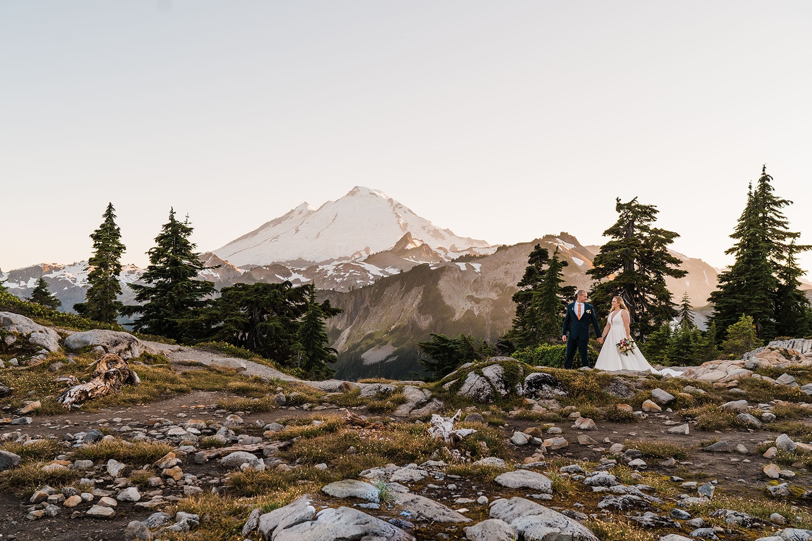 Bride and groom hold hands while walking across a mountain trail in the North Cascades.