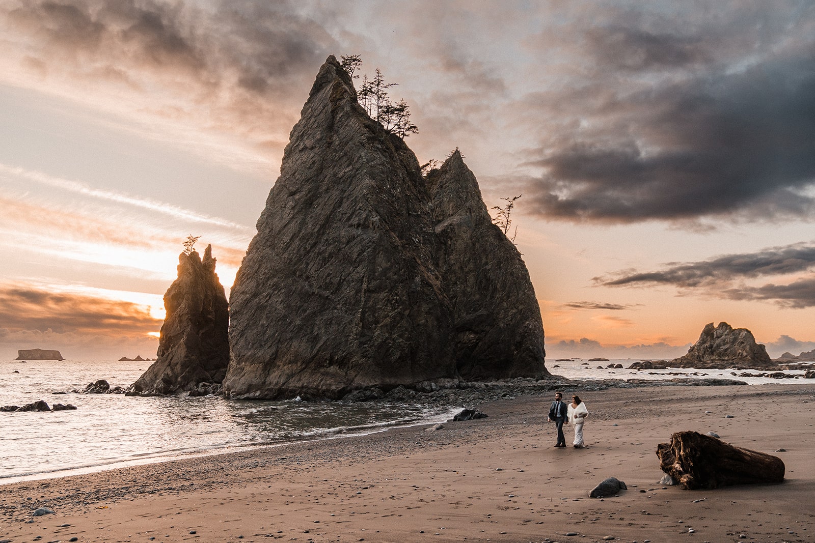 Bride and groom hold hands while walking across Rialto beach on the Olympic Peninsula, one of the best places to elope in Washington.