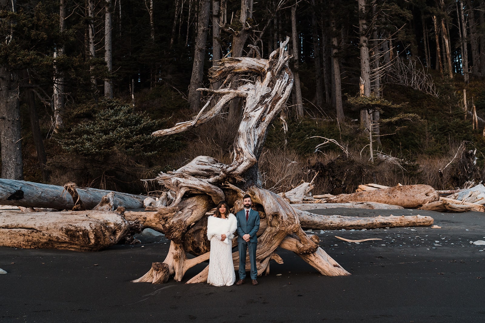 Bride and groom stand on a black sand beach in Olympic National Park during their elopement adventure photo session.