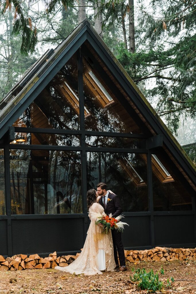 Bride and groom kiss in front of A-Frame cabin at elopement in Snoqualmie