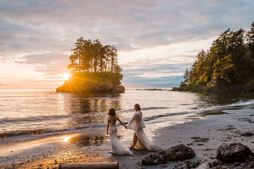 Two brides hold hands and walk across the beach during their Washington state elopement in Olympic National Park