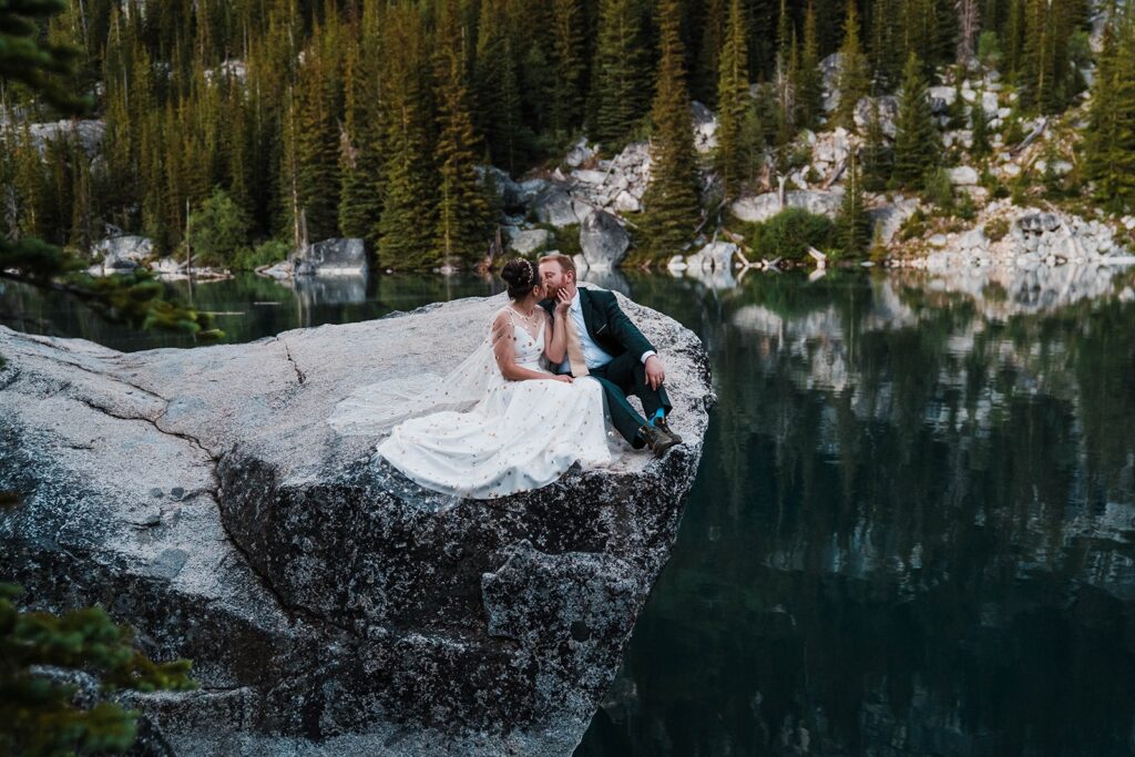 Bride and groom kiss on a granite rock overlooking an alpine lake at their Washington state elopement in Leavenworth