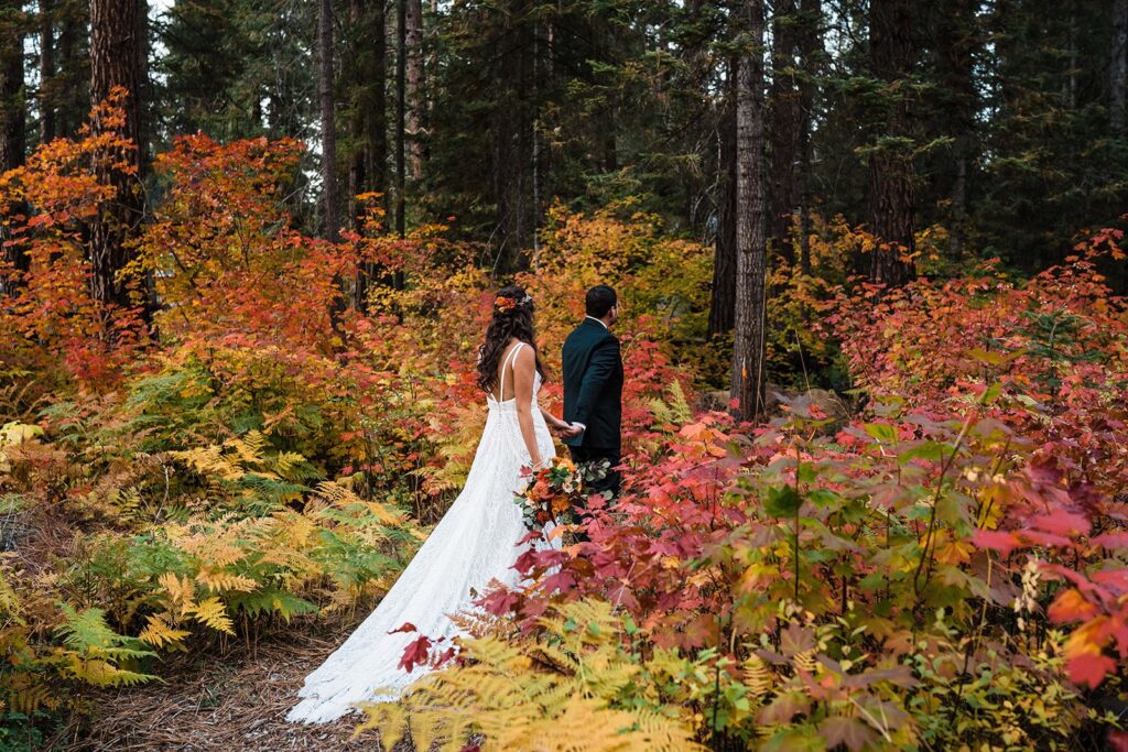 Bride and groom hold hands while walking through the forest during their fall elopement in Leavenworth