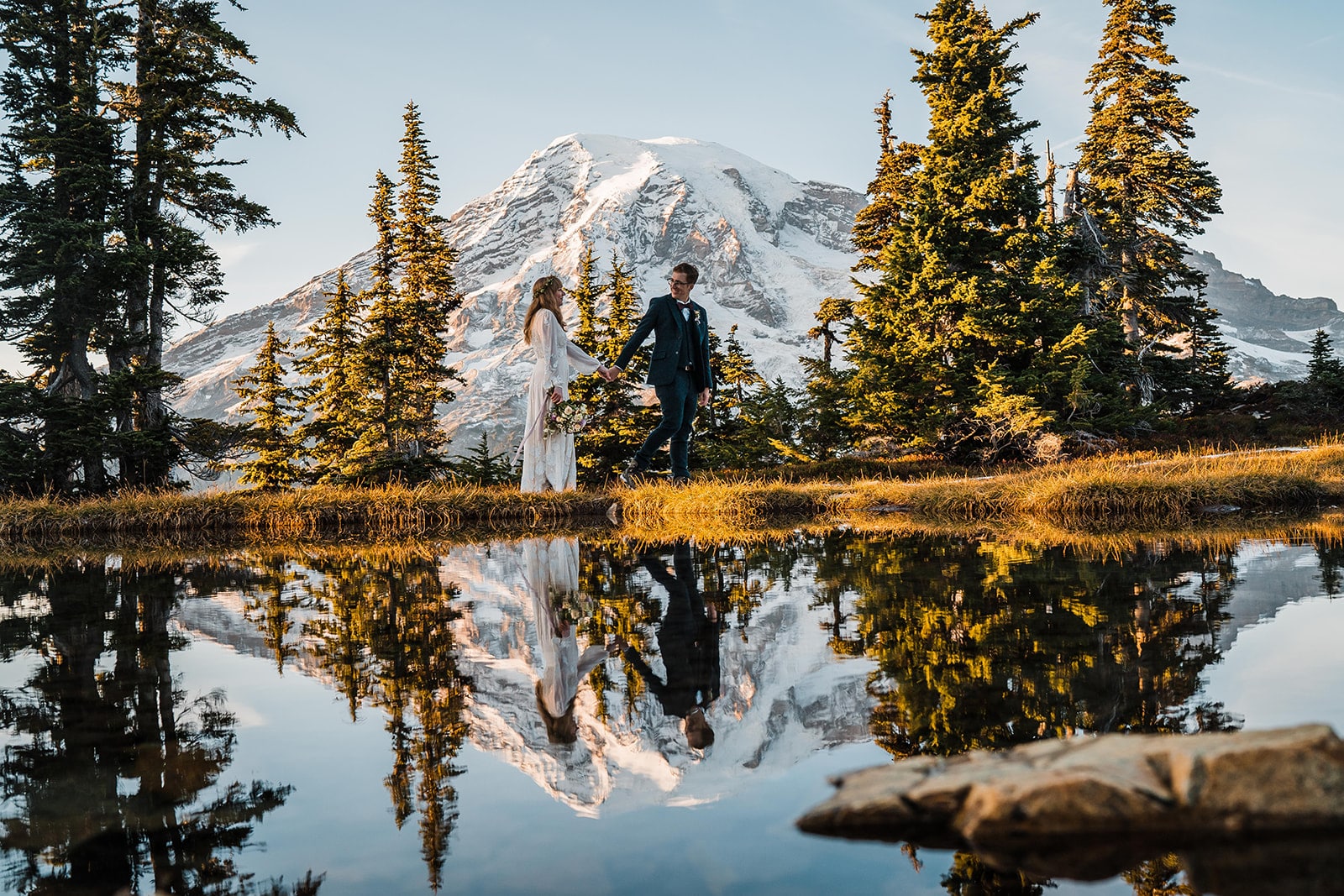 Bride and groom hold hands while walking in front of an alpine lake at Mt Rainier National Park, one of the best Washington state elopement locations.