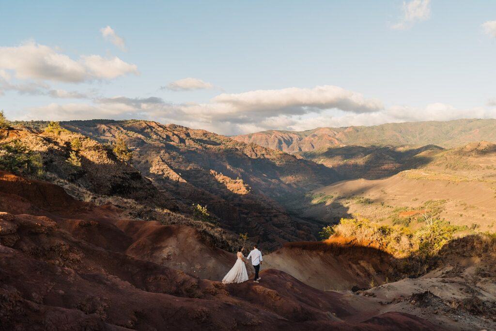 Bride and groom hold hands while walking through the red rock canyons at their Kauai mountain elopement