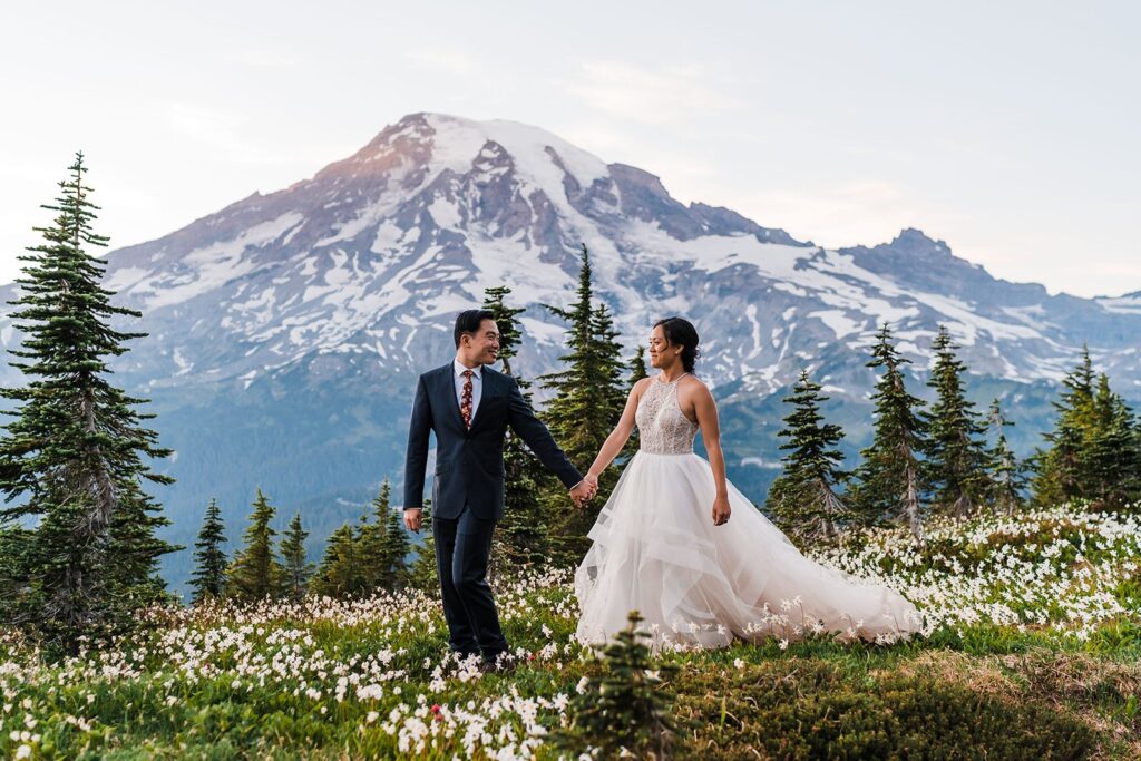 Bride and groom hold hands while walking through the wildflowers at their Mt Rainier mountain elopement