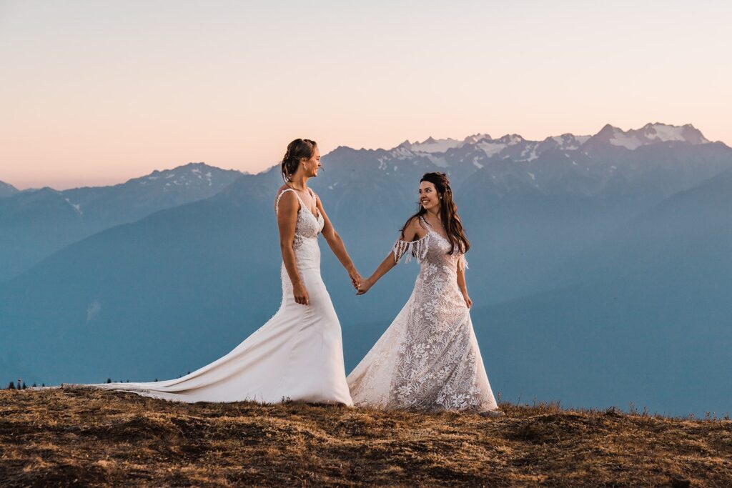 Two brides hold hands while walking across Hurricane Ridge during their Washington mountain elopement