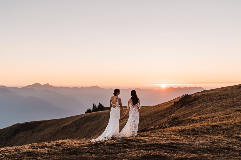 Two brides hold hands while walking across Hurricane Ridge during their Washington mountain elopement