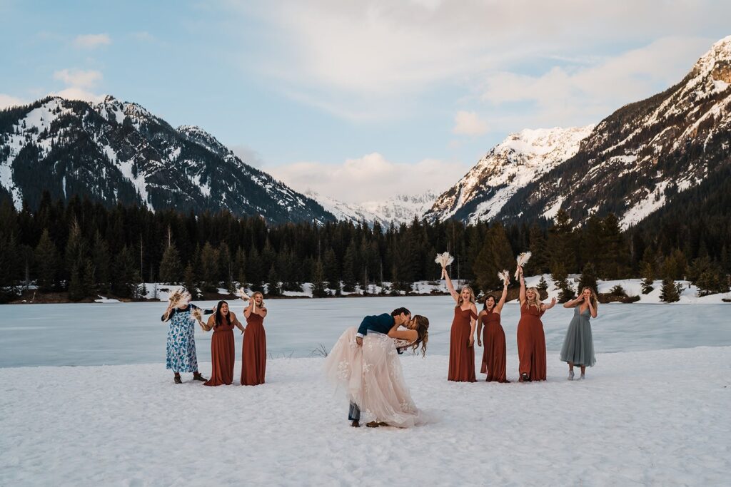 Brides kiss while bridesmaids cheer in the background at their mountain elopement ceremony in Snoqualmie