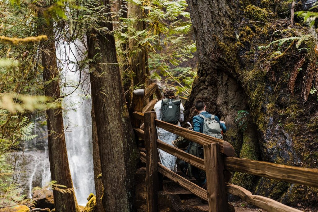 Bride and groom hike up wooden stairs toward Merymere Falls at their spring elopement in Washington. 