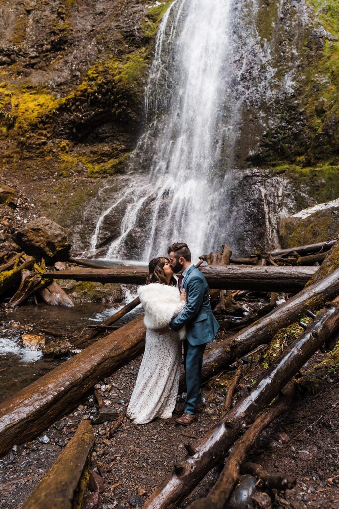 Bride and groom kiss at the base of Marymere Falls at their spring elopement in Washington