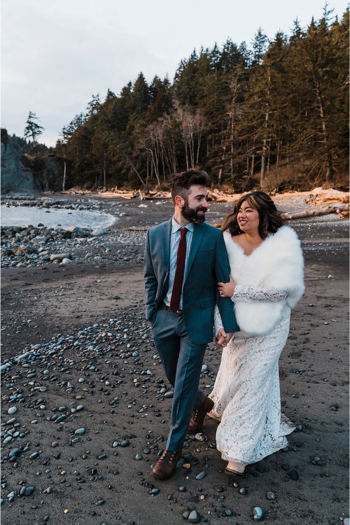 Bride and groom hold hands while walking across the beach at their spring elopement in Washington