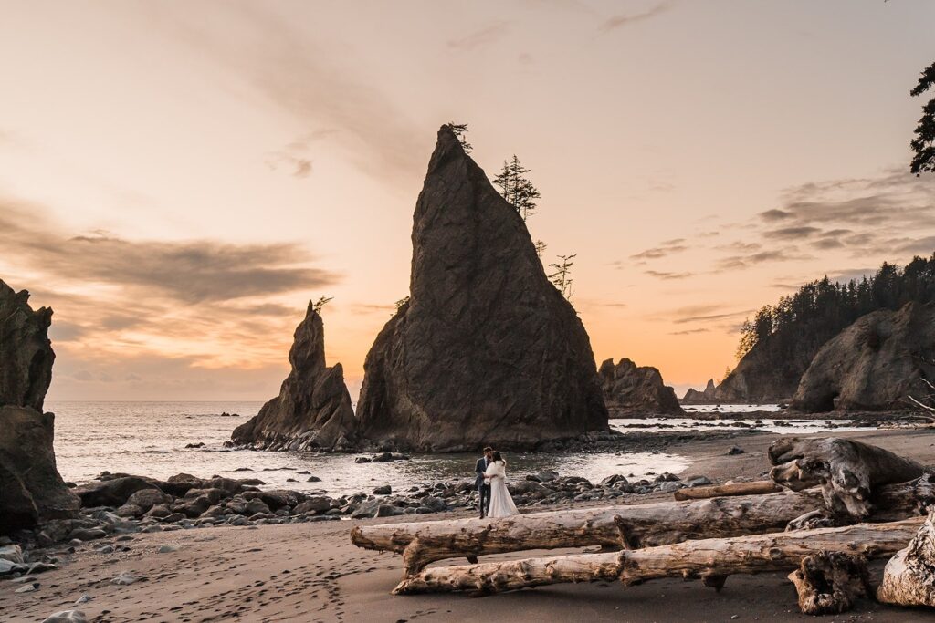 Bride and groom kiss on a pile of driftwood at Rialto Beach for their sunset elopement photos