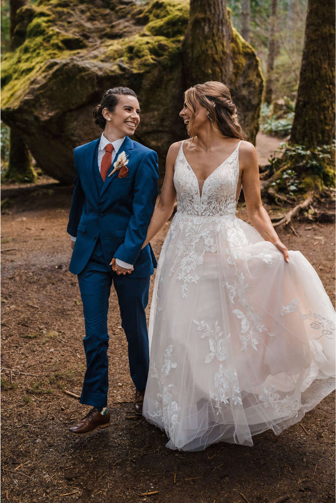 Two brides hold hands and laugh while walking through a forest in Snoqualmie