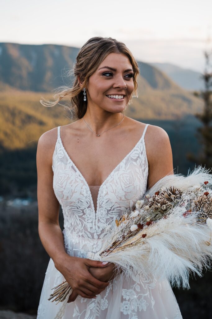 Bride wearing white wedding dress and holding dried floral bouquet on top of a mountain in Snoqualmie