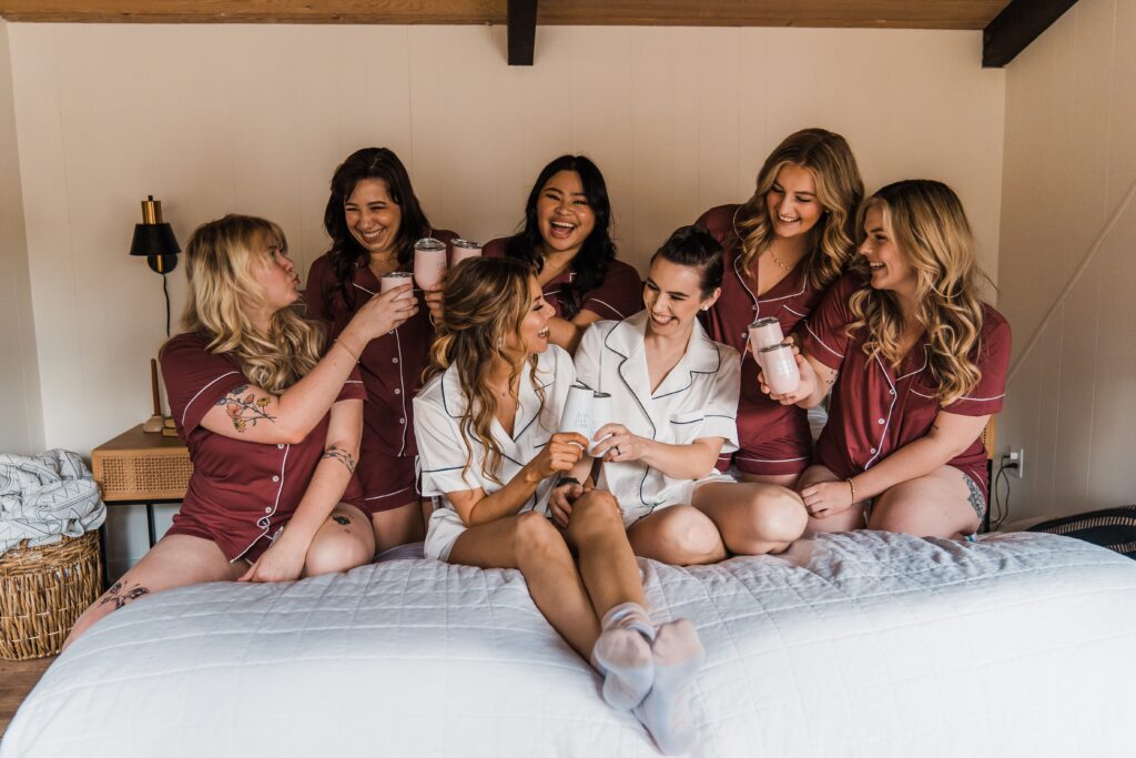 Brides and bridesmaids sit on a bed in matching night shirts