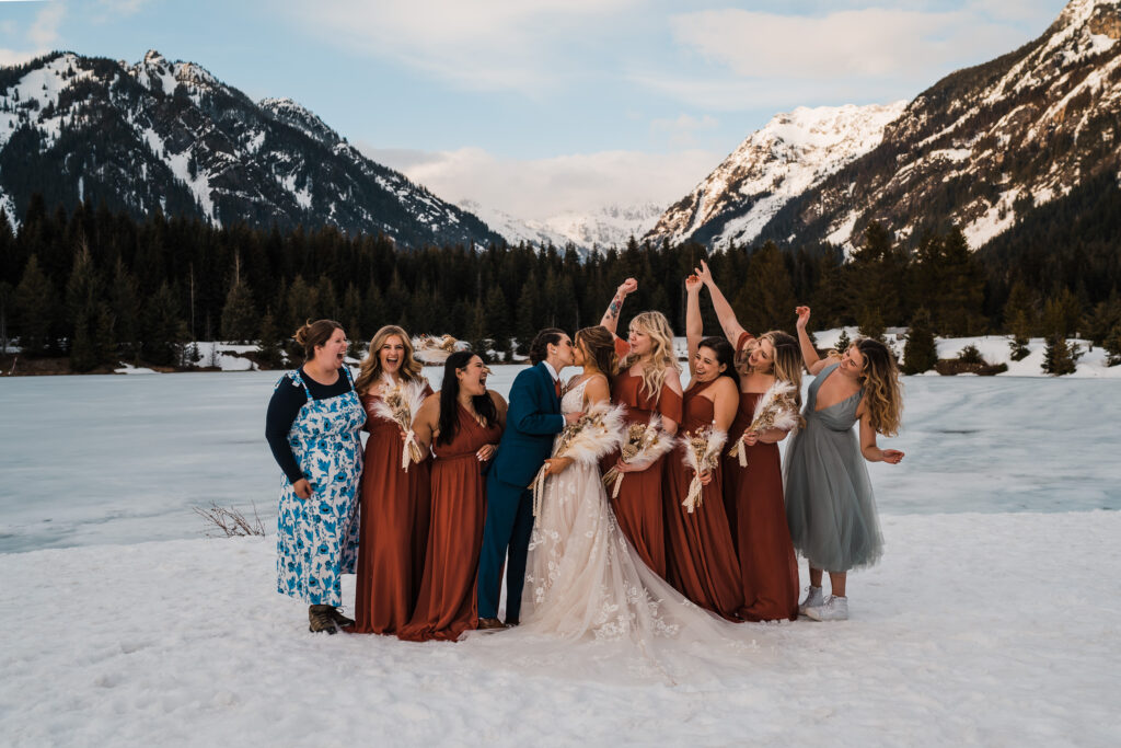 Brides kiss while bridesmaids and friends cheer