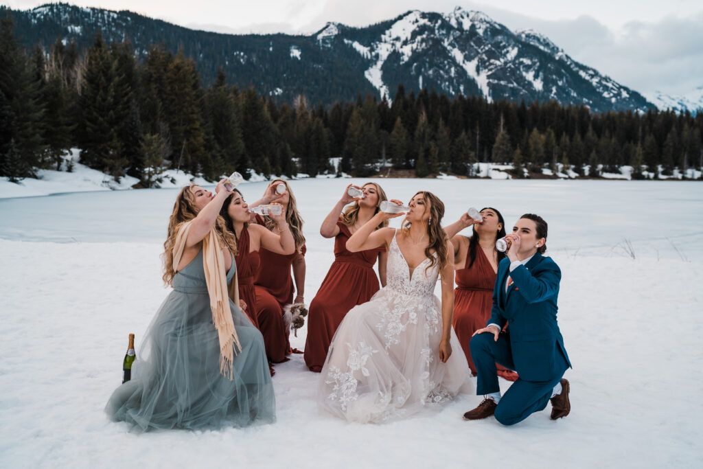Brides drink with friends and bridesmaids while kneeling in the snow