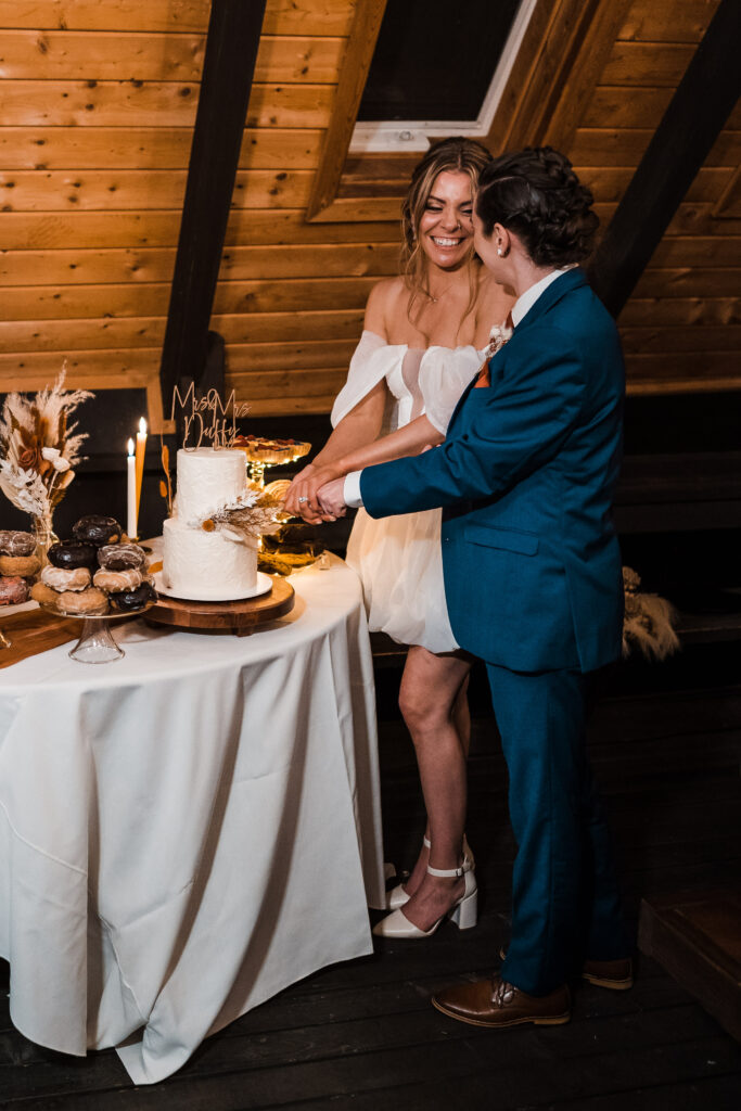 Brides laugh while cutting their cake at their adventure wedding dinner reception