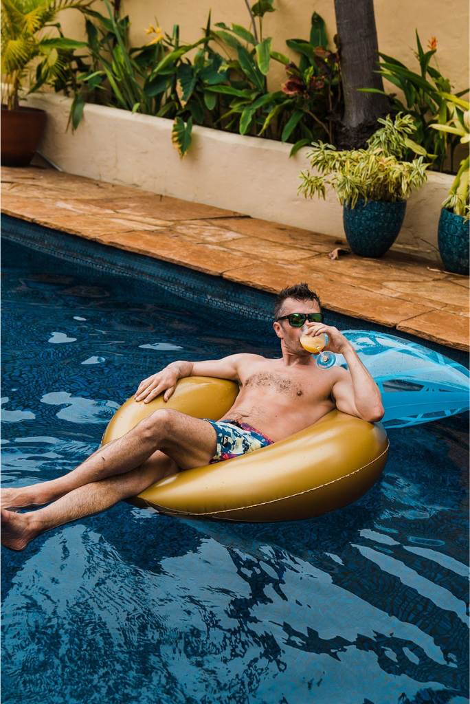Groom lounges in the pool sipping a mai tai drink before getting ready for his Maui elopement
