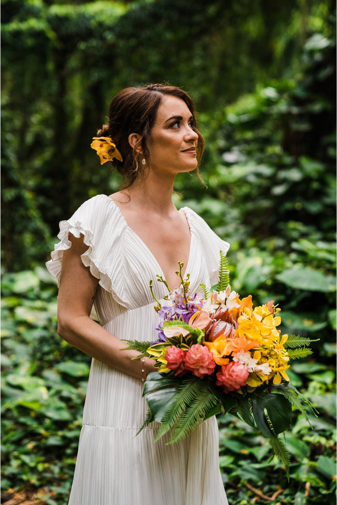 Bride wearing white dress and holding colorful flowers in the rainforest during her Maui elopement