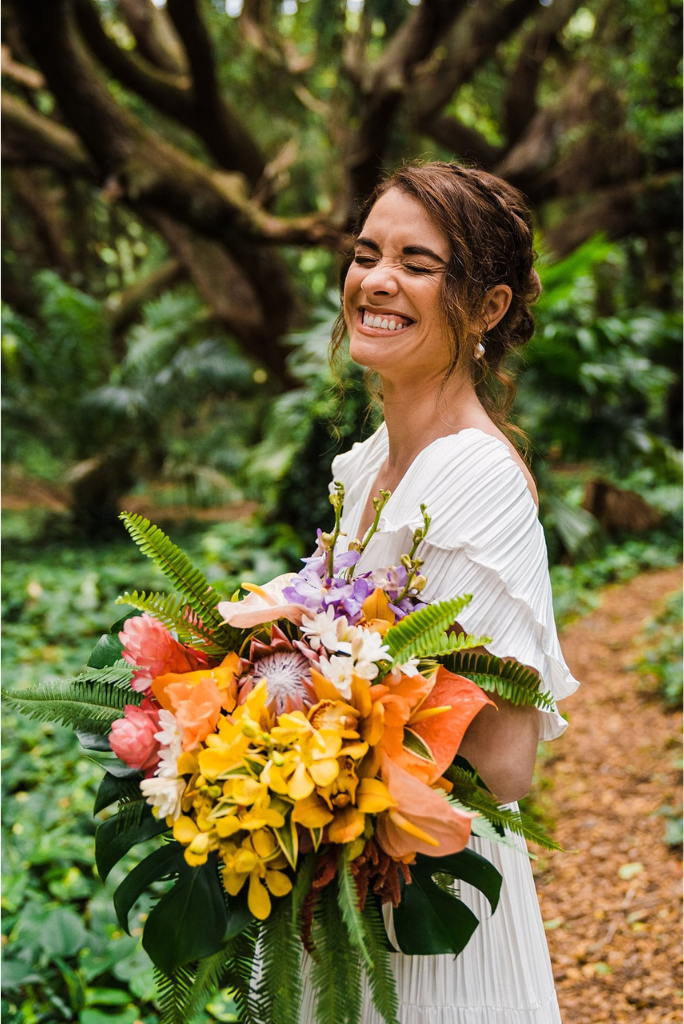 Bride wearing white dress and holding colorful flowers in the rainforest during her Maui elopement