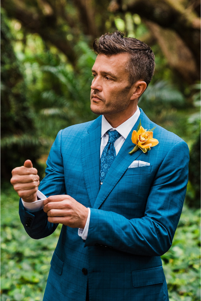 Groom wearing a blue suit and a yellow boutonniere in the rainforest