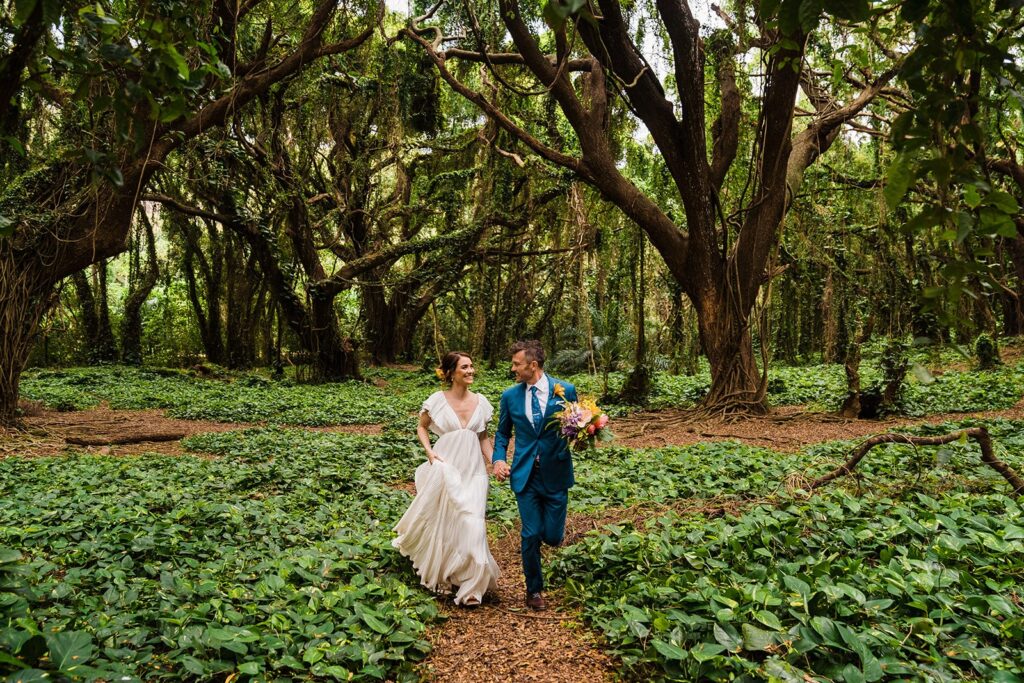 Bride and groom hold hands while walking through the rainforest at their Hawaii elopement