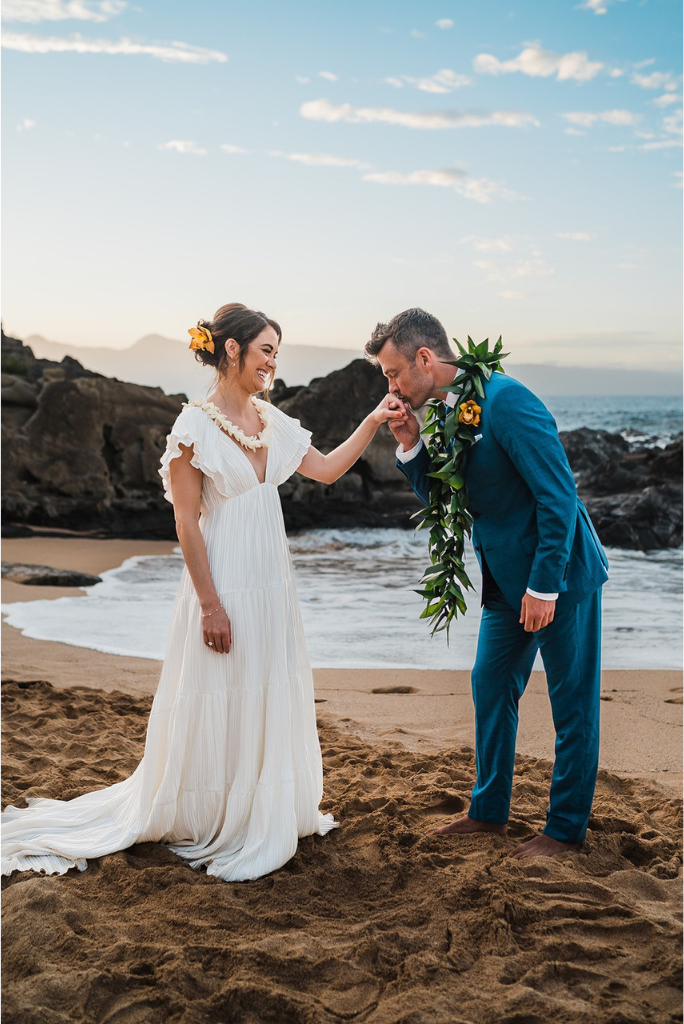 Groom kisses bride's hand during Hawaii elopement ceremony on the beach