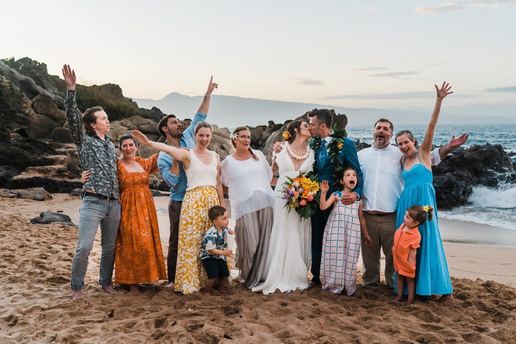 Guests cheer while bride and groom kiss on the beach after their Hawaii elopement ceremony