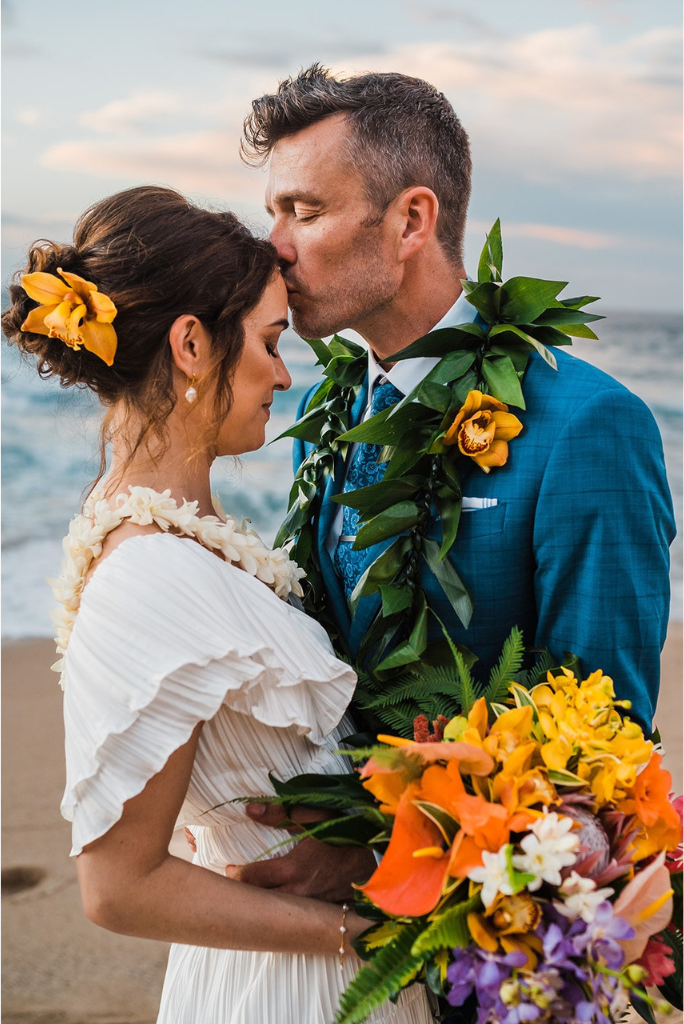 Groom kisses bride on the forehead after intimate beach elopement in Maui