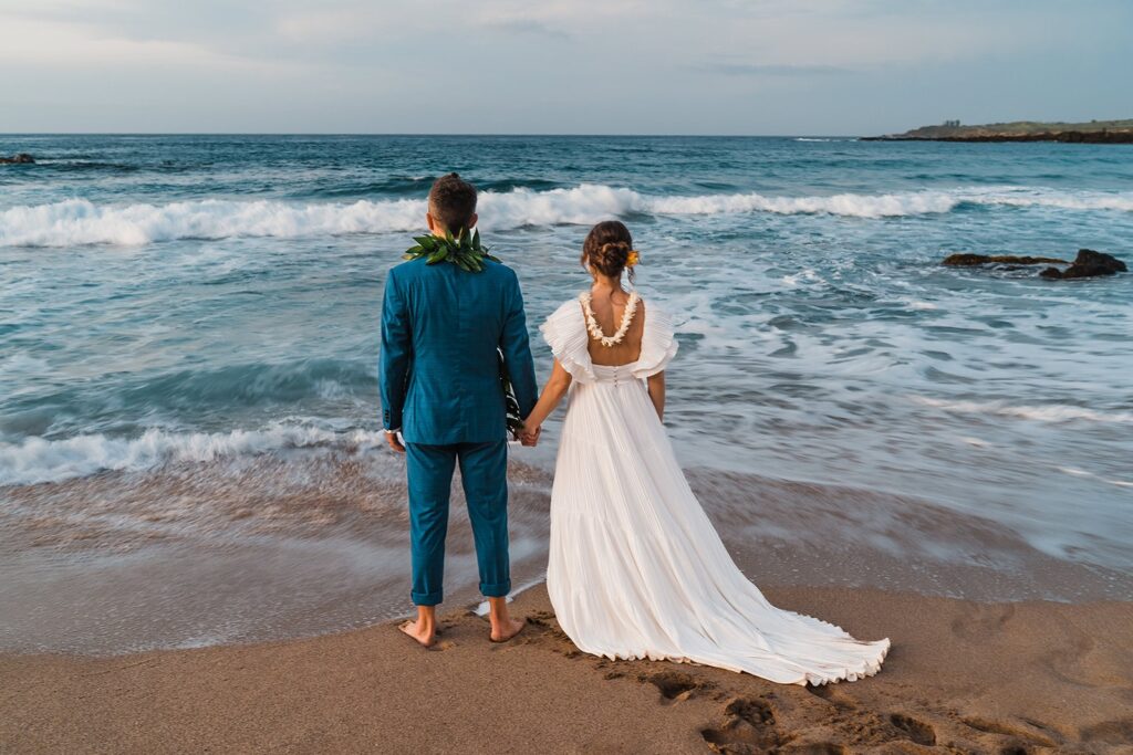 Bride and groom stand by the ocean during their sunset photos on the beach