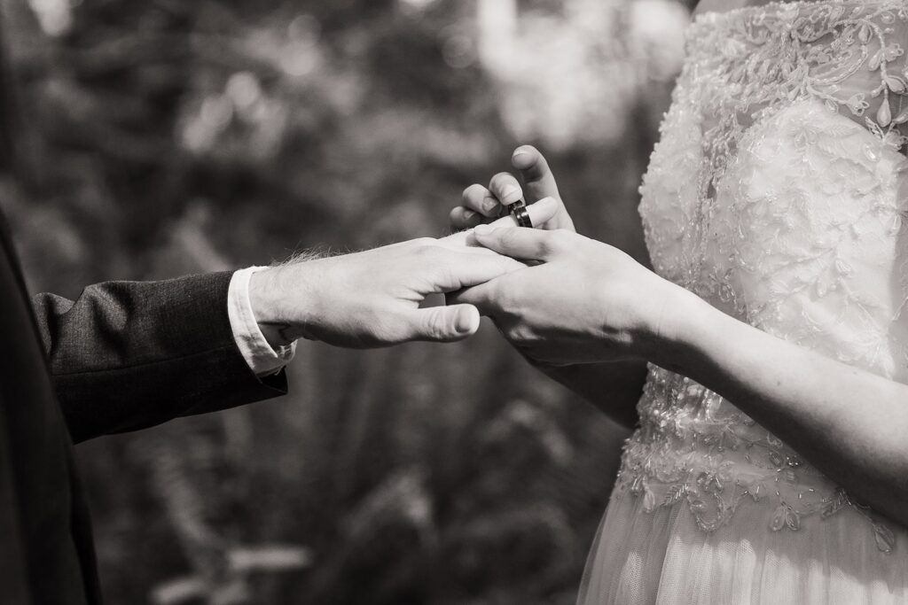 Bride puts wedding band on groom's hand during redwoods elopement ceremony
