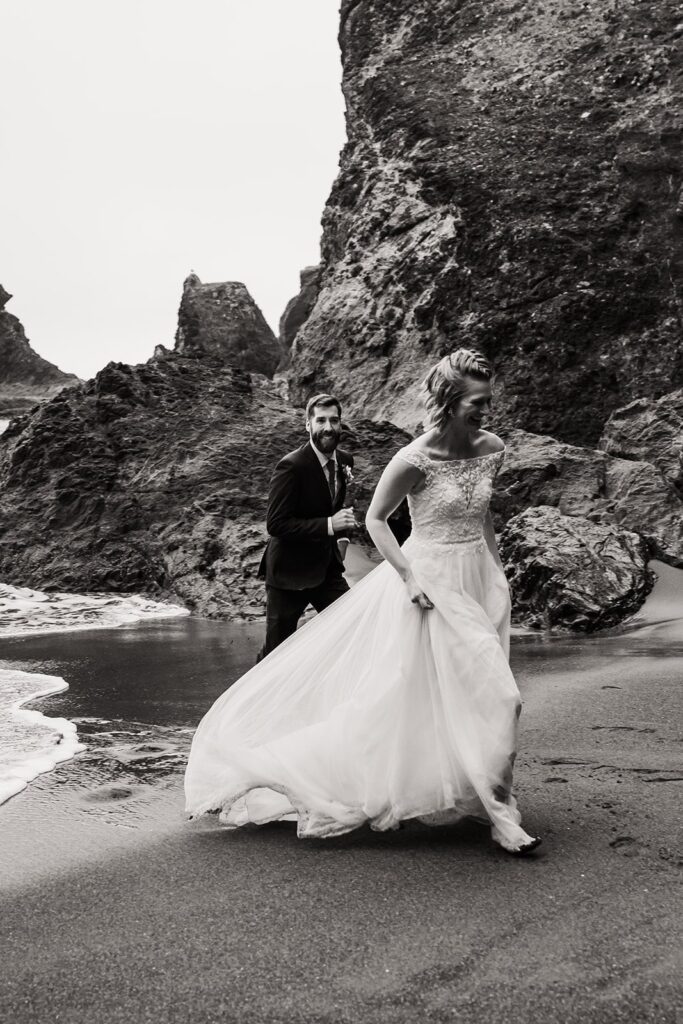 Bride and groom run away from the waves at their beach elopement in Oregon