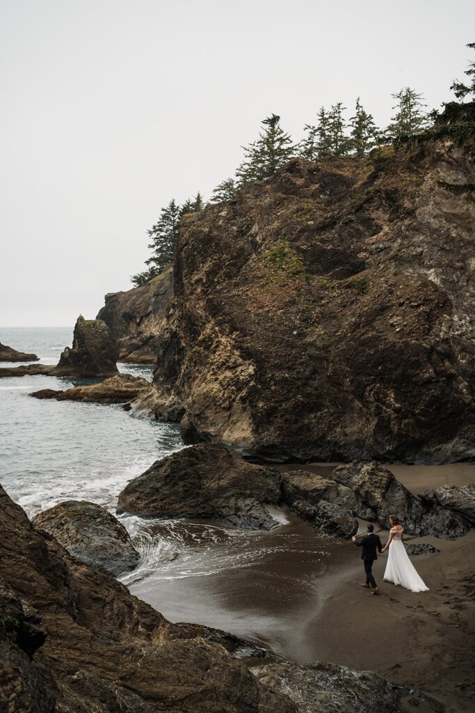 Bride and groom hold hands while walking toward the ocean during their beach elopement photos in Oregon