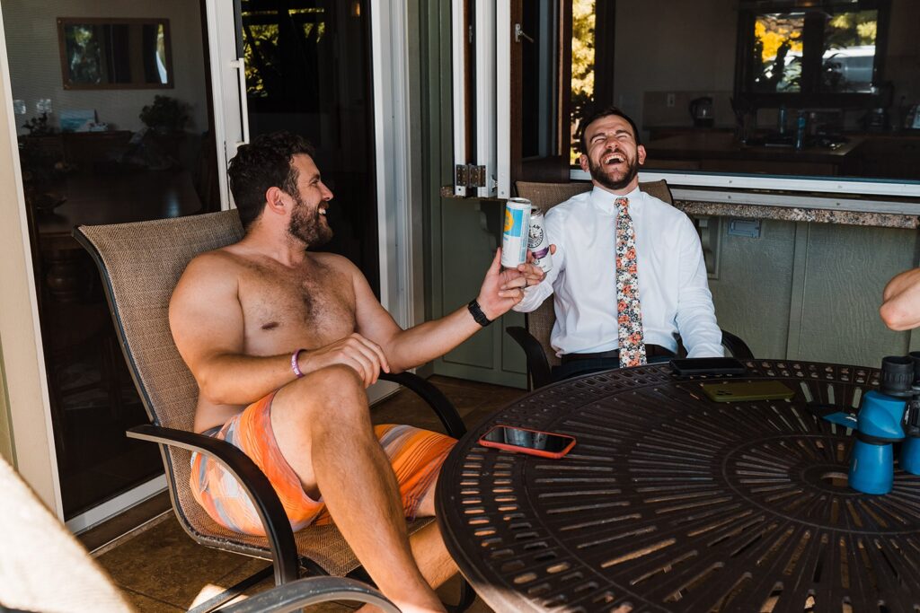 Groom and friend toasting and laughing on the porch before two-day wedding on Kauai