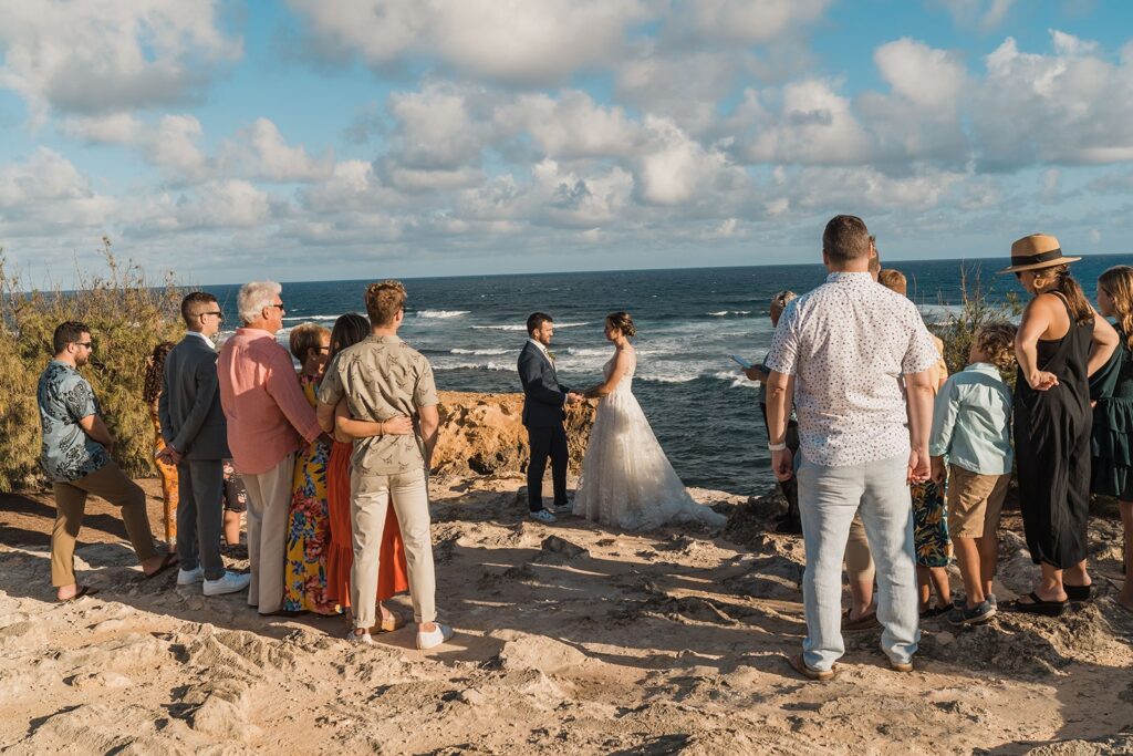 Bride and groom hold hands while family and friends watch their Kauai wedding ceremony 