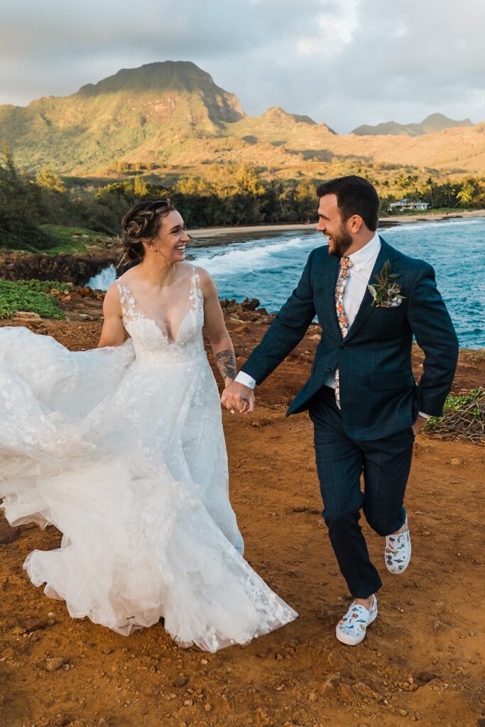 Bride and groom hold hands while running around on the cliffs at their wedding on Kauai