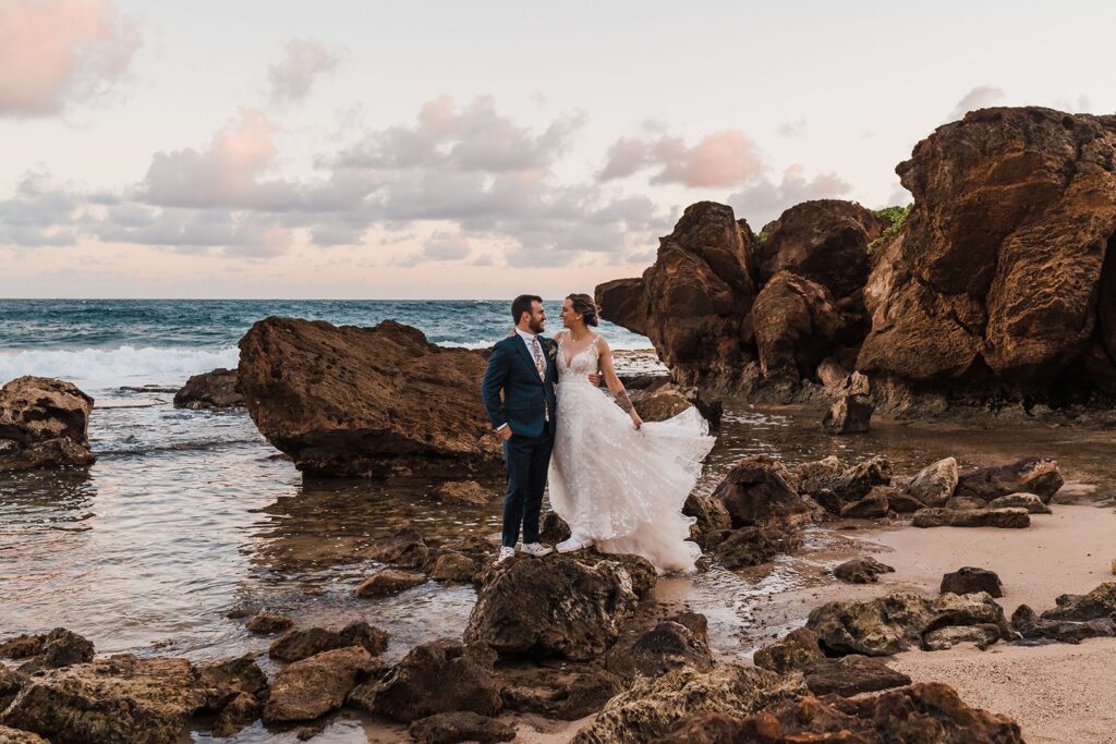 Bride and groom stand on a rock on the coast for their Kauai wedding photos